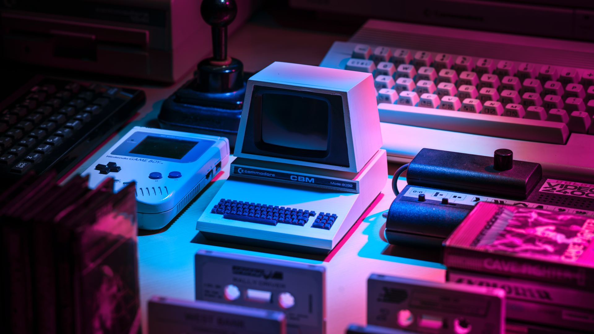 Retro-Computer und Spielkonsole, umgeben von Kassetten und Games, beleuchtet in Blau und Pink