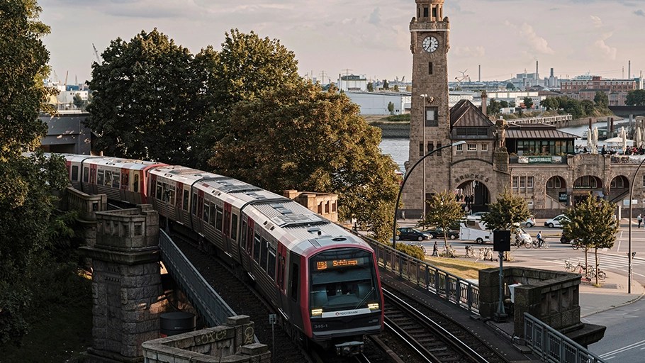 A train of the Hamburg U-Bahn emerging from a bridge, with the historic Landungsbrücken building and clock tower in the background.
