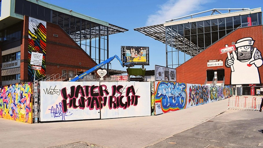 Graffiti-covered construction site near the Millerntor-Stadion, home of FC St. Pauli, with a bold "Water is a Human Right" mural.