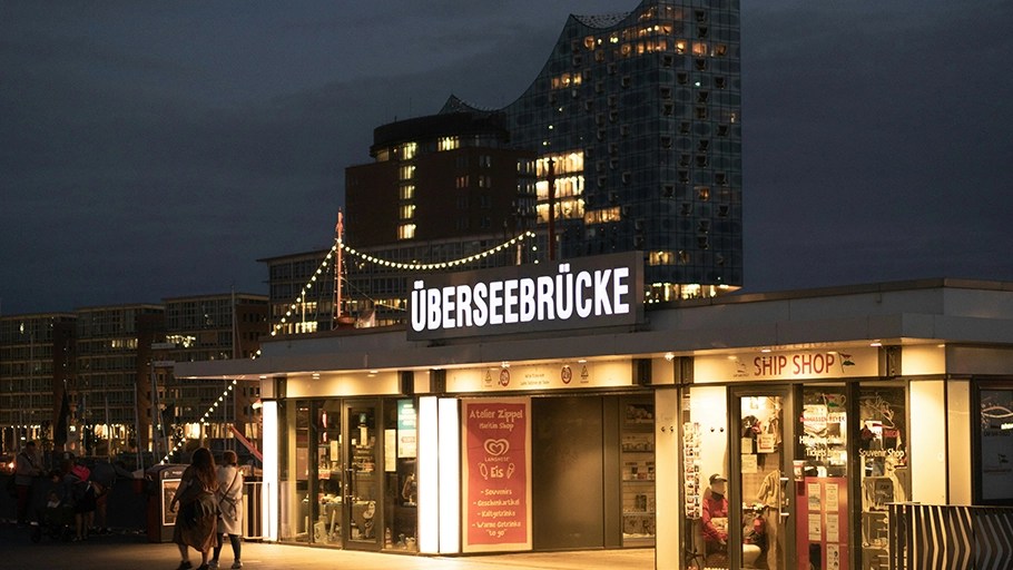The Überseebrücke at night, with the illuminated Elbphilharmonie visible in the background.