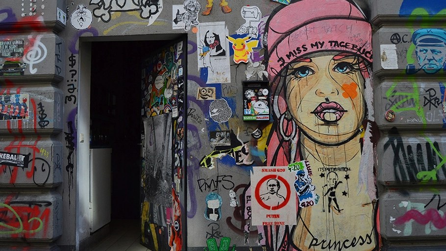 A graffiti-covered entrance of a building in Hamburg, featuring street art, stickers, and a mural of a woman with pink hair.